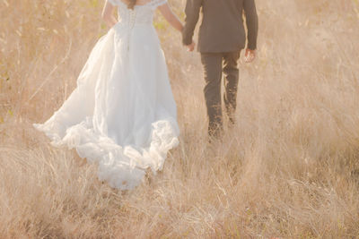 Rear view of wedding couple holding hands while walking at farm