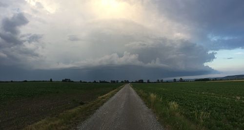 Empty road amidst field against sky