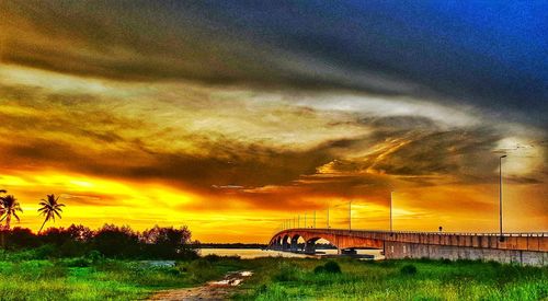 Cars on bridge against dramatic sky during sunset