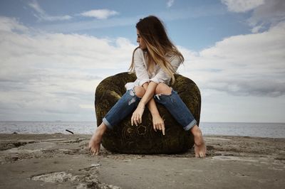 Young woman sitting on beach against sky