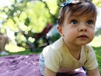 Close-up of cute baby girl looking away while kneeling on blanket at park