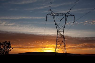 Low angle view of silhouette electricity pylons against orange sky