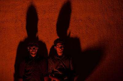 Portrait of men standing against wall at illuminated room