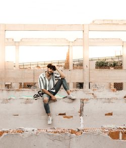 Full length of young man sitting on retaining wall in old ruins