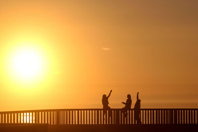 Silhouette people by railing against orange sky