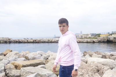 Portrait of young man standing on rock by sea against sky