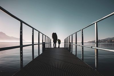 Rear view of man standing on bridge over sea against sky