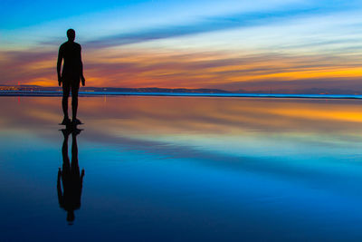 Rear view of silhouette statue standing at beach against sky