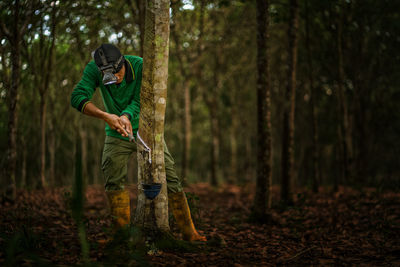 Man standing by tree trunk in forest