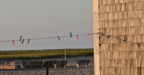 Clothespins hanging from string by benches at beach against clear sky