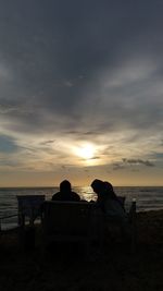 Rear view of men sitting on beach against sky during sunset