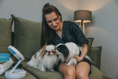 Portrait of young woman with dog sitting on sofa at home