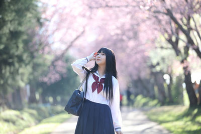 Young woman looking away while standing against cherry tree