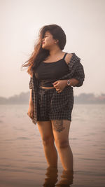 Beautiful young woman standing at beach during sunset