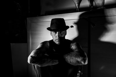 Portrait of man wearing hat sitting by cabinet at home