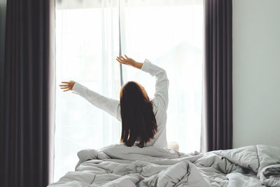 Rear view of woman lying on bed at home