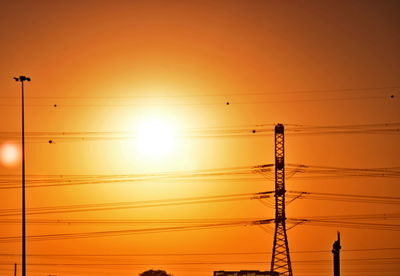 Low angle view of silhouette electricity pylon against orange sky