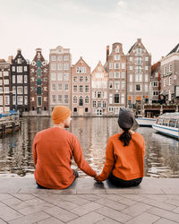 Rear view of couple sitting by canal against buildings in city