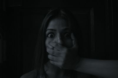 Portrait of shocked woman with mouth covered by hand in darkroom