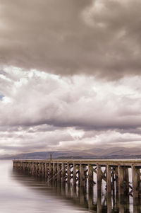 Bridge over calm lake against clouds