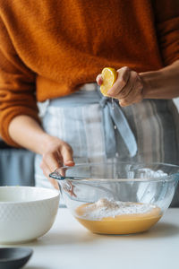 Glass bowl with orange vegetable mixture in hands of crop cook squeezing ripe lemon into puree at table