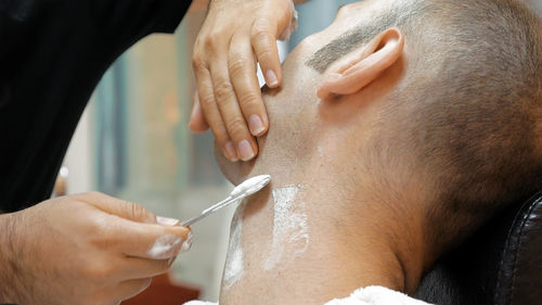 Cropped hands of barber shaving man