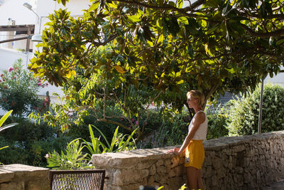 Side view of young woman standing against tree