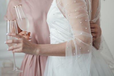Midsection of bridesmaid and bride holding champagne flute