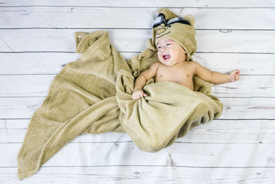 Smiling baby boy wrapped in blanket while lying on wood
