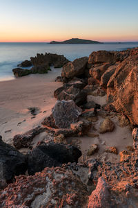 Rocks on beach against sky during sunset