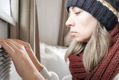 Young frozen woman wearing a sweater freezing for winter cold at home. girl is near electric heater.
