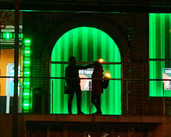 Rear view of man and woman standing in illuminated building
