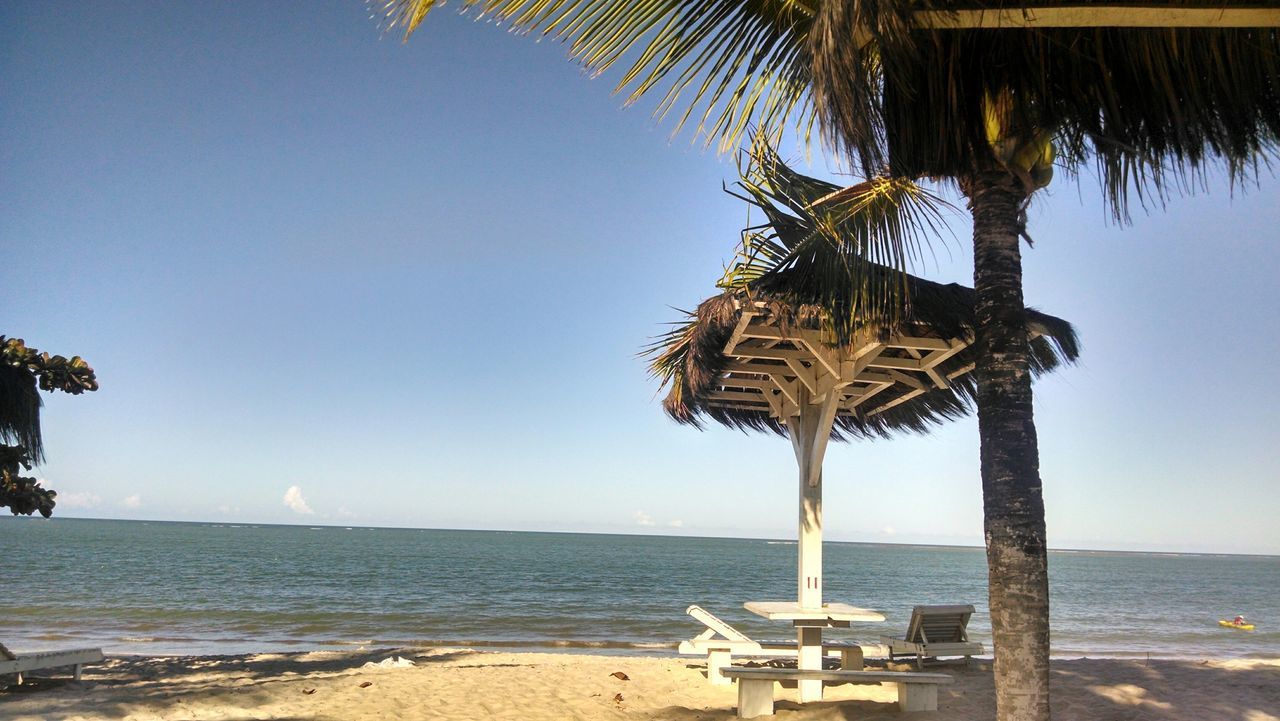 sea, beach, clear sky, water, horizon over water, sand, tranquility, shore, tranquil scene, beach umbrella, scenics, palm tree, thatched roof, nature, beauty in nature, copy space, vacations, parasol, lounge chair, blue