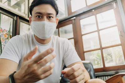 Man influencer with mask is talking with his camera in a cafe.