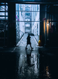 Woman walking on wet street amidst buildings in city