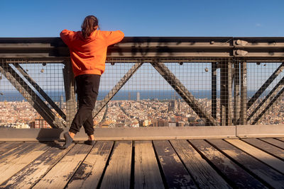 Rear view of girl standing by railing against sky in city