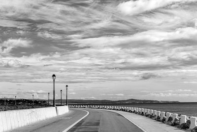 Empty road along street lights against sky