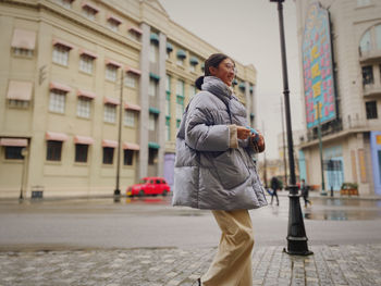 Side view of young woman standing on street in city