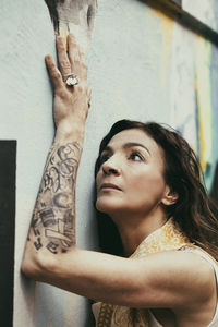 Woman looking away while standing against wall