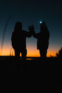 Silhouette friends standing against sky during sunset