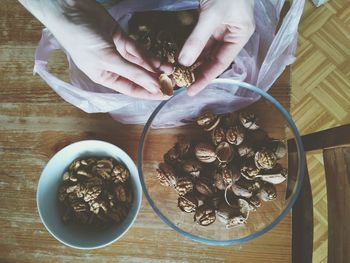 Cropped hands of woman removing shells of walnut on table