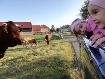 Cute sisters leaning on car window at farm by cattle