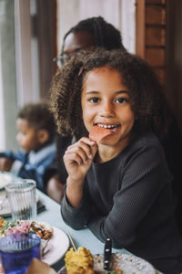 Portrait of smiling girl eating nacho chip sitting at restaurant