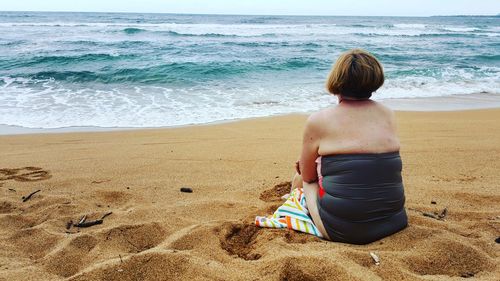 Rear view of woman in swimwear sitting at sandy beach