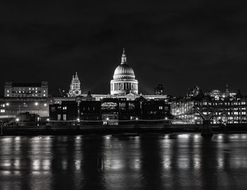 Illuminated buildings by river in city at night