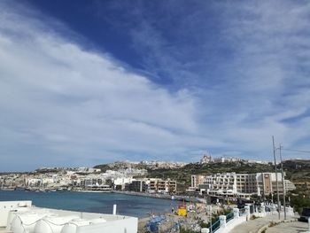 Sailboats in city by sea against sky