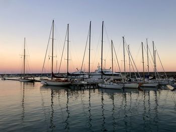 Sailboats moored in harbor at sunset