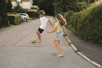 Brother and sister enjoying while playing with soccer ball on road