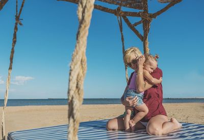 Mother and daughter embracing at beach against blue sky