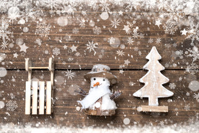 Snowman against wooden wall during snowfall